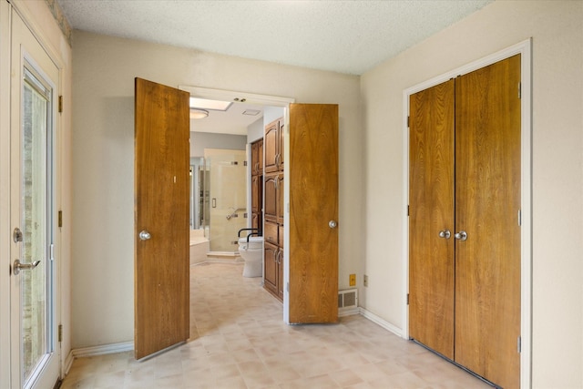 unfurnished bedroom featuring visible vents, baseboards, light floors, ensuite bathroom, and a textured ceiling