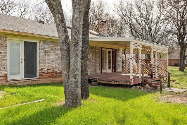 rear view of house featuring a chimney, french doors, a deck, a lawn, and brick siding