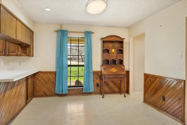 dining area featuring a wainscoted wall, a textured ceiling, light floors, and wallpapered walls