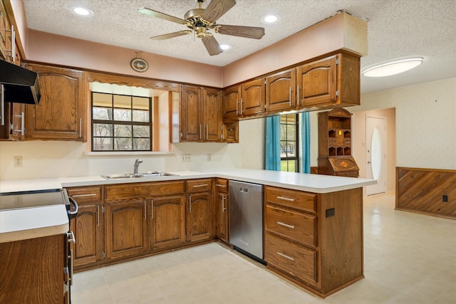 kitchen featuring light floors, brown cabinets, a peninsula, stainless steel dishwasher, and a sink