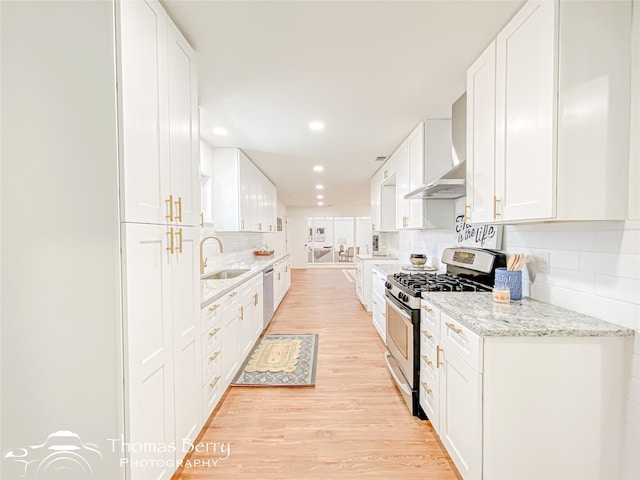 kitchen featuring a sink, stainless steel appliances, white cabinetry, wall chimney range hood, and light wood-type flooring