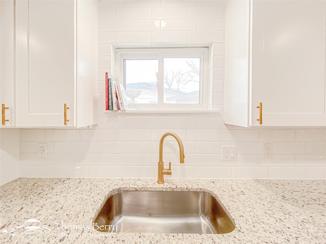 details featuring a sink, decorative backsplash, light stone counters, and white cabinetry