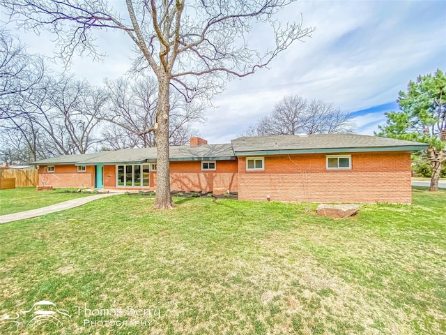 back of property featuring brick siding, a lawn, fence, and a chimney