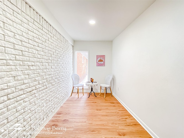 living area with light wood finished floors, brick wall, and baseboards