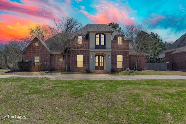 french country home featuring stucco siding, a lawn, fence, french doors, and brick siding