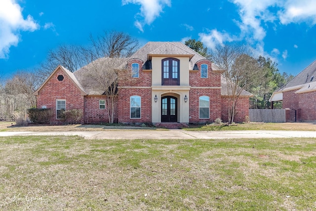 french provincial home featuring french doors, brick siding, a front yard, and fence