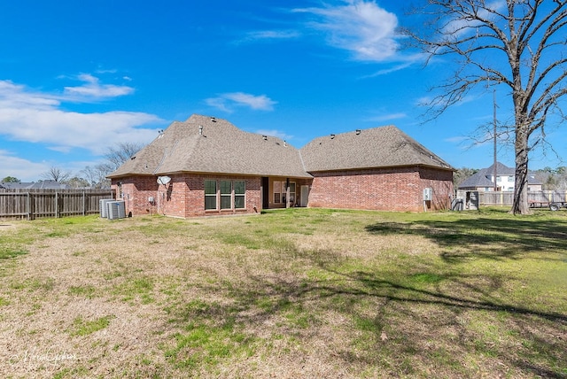 back of house featuring brick siding, central AC, fence private yard, and a lawn