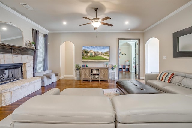 living room with wood finished floors, arched walkways, a fireplace, crown molding, and ceiling fan