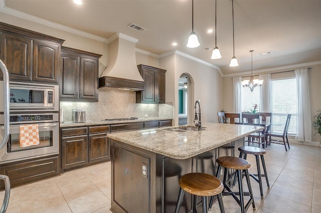 kitchen with visible vents, premium range hood, light stone counters, stainless steel appliances, and a sink