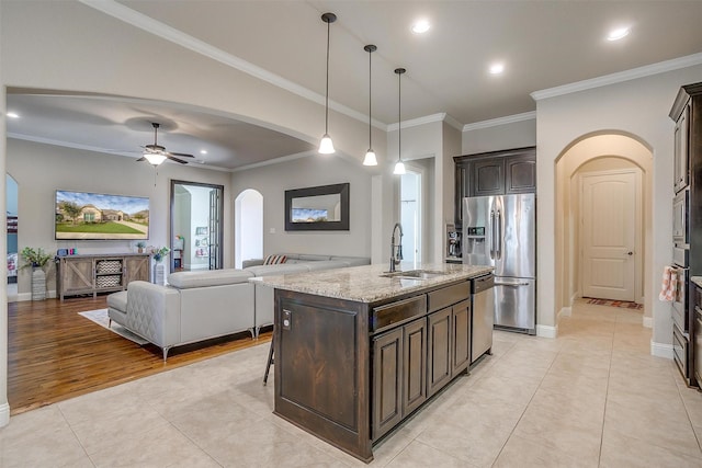 kitchen featuring dark brown cabinetry, light tile patterned floors, appliances with stainless steel finishes, arched walkways, and a sink