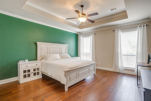 bedroom with visible vents, baseboards, a tray ceiling, ornamental molding, and hardwood / wood-style flooring