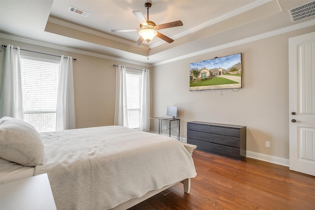 bedroom featuring a tray ceiling, wood finished floors, visible vents, and ornamental molding