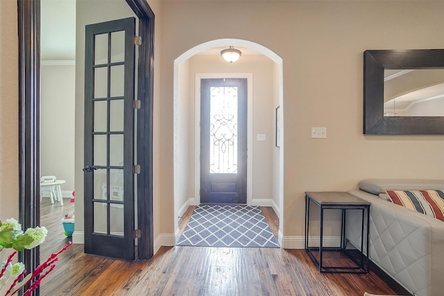 entryway featuring baseboards, arched walkways, and wood finished floors