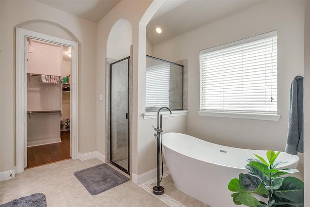 full bath with tile patterned floors, a walk in closet, a shower stall, baseboards, and a freestanding bath