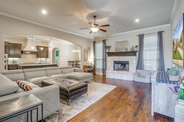 living room featuring a fireplace, arched walkways, ceiling fan, dark wood-type flooring, and crown molding