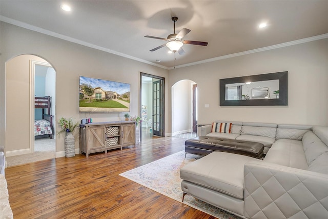 living room with wood finished floors, arched walkways, ceiling fan, and ornamental molding