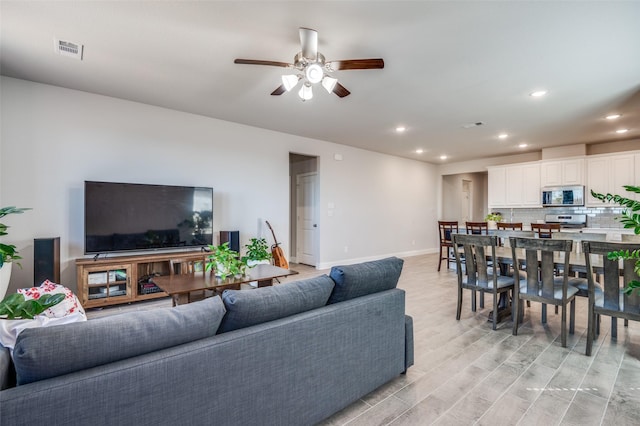 living area featuring visible vents, baseboards, ceiling fan, light wood-type flooring, and recessed lighting