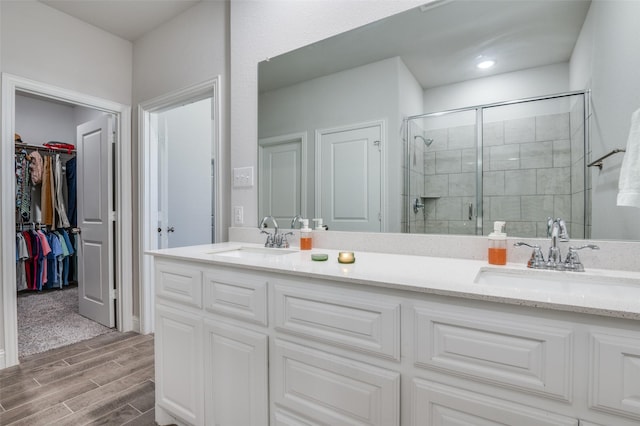 bathroom featuring double vanity, wood finish floors, a stall shower, and a sink