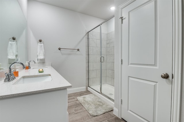 bathroom with a sink, double vanity, baseboards, a shower stall, and wood tiled floor