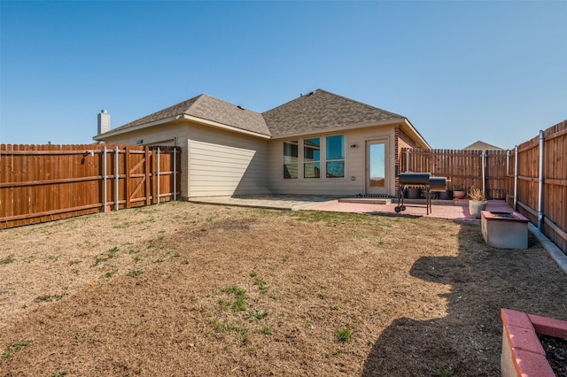 back of house with a shingled roof, a fenced backyard, a lawn, and a patio area