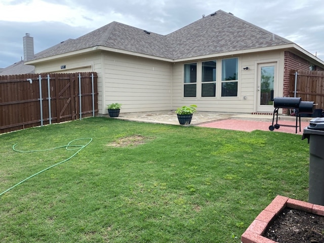 back of property with a garage, fence, a patio, a shingled roof, and a lawn