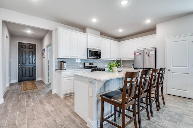 kitchen featuring appliances with stainless steel finishes, light wood finished floors, light countertops, a breakfast bar area, and white cabinetry