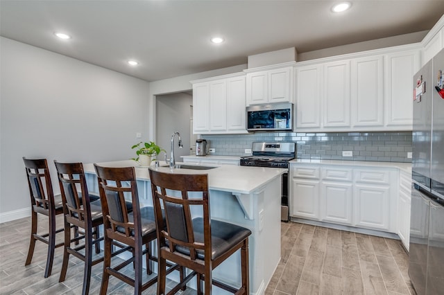 kitchen with a sink, a center island with sink, stainless steel appliances, and light wood-type flooring