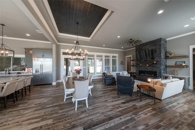 dining space featuring baseboards, dark wood finished floors, recessed lighting, a stone fireplace, and ceiling fan with notable chandelier