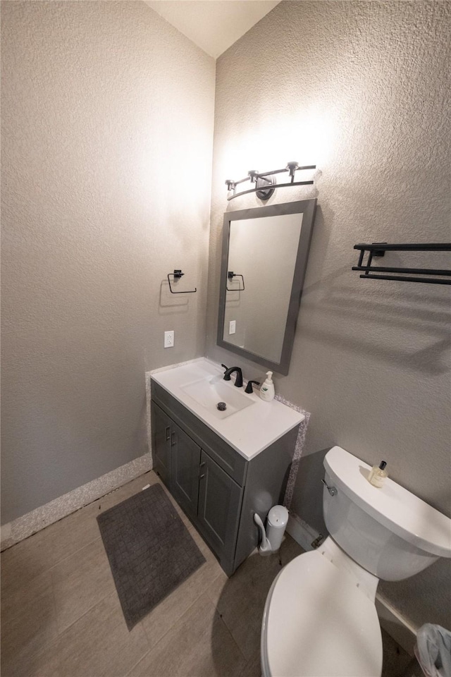 half bath with toilet, vanity, and a textured wall