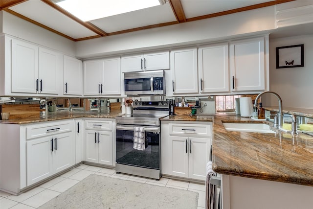 kitchen with dark stone counters, light tile patterned flooring, white cabinets, stainless steel appliances, and a sink