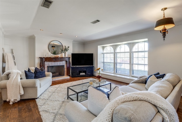 living room featuring visible vents, a fireplace with raised hearth, crown molding, and wood finished floors