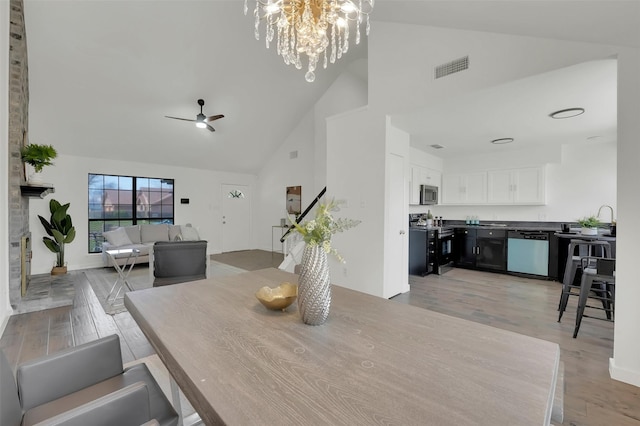 dining area featuring visible vents, ceiling fan with notable chandelier, high vaulted ceiling, and light wood-style floors