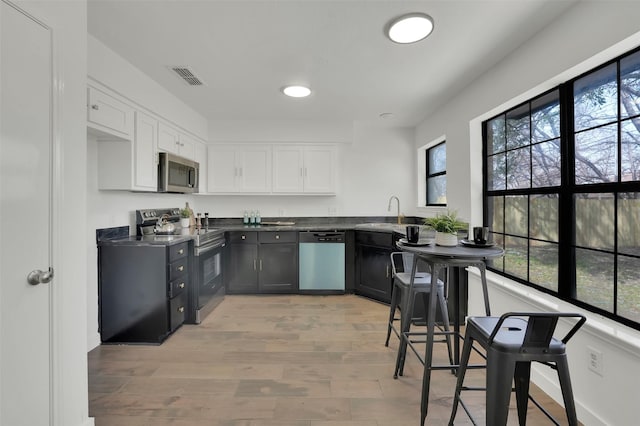 kitchen featuring visible vents, a sink, dark countertops, stainless steel appliances, and white cabinets