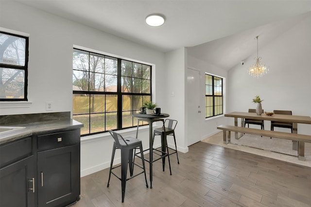 dining area featuring a chandelier, plenty of natural light, vaulted ceiling, and wood finished floors