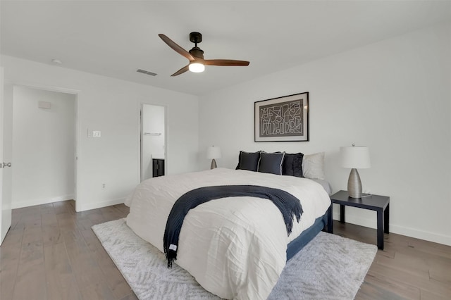 bedroom with a ceiling fan, wood finished floors, visible vents, baseboards, and ensuite bath