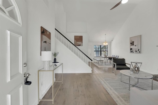 foyer entrance with a ceiling fan, high vaulted ceiling, wood finished floors, and stairs