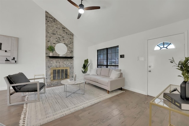 living area with baseboards, a fireplace, wood finished floors, high vaulted ceiling, and a ceiling fan