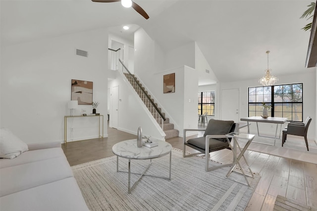 living area with visible vents, stairway, ceiling fan with notable chandelier, wood finished floors, and high vaulted ceiling