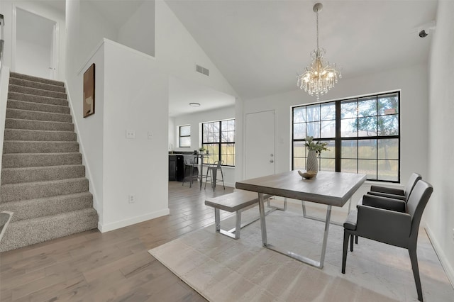 dining area featuring visible vents, a chandelier, stairs, wood finished floors, and high vaulted ceiling