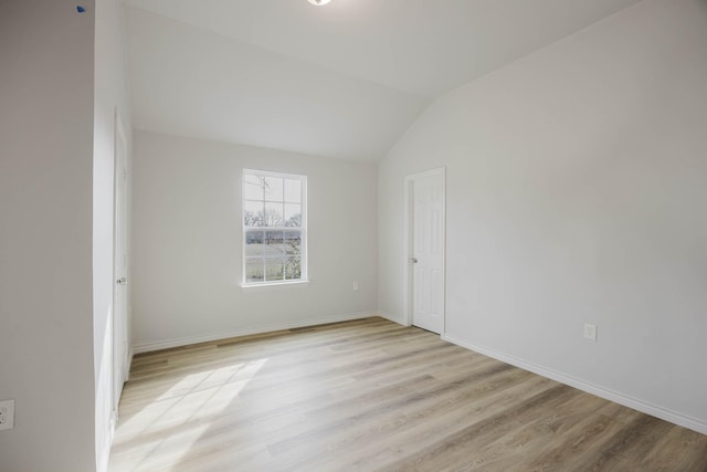 spare room featuring baseboards, light wood-type flooring, and lofted ceiling