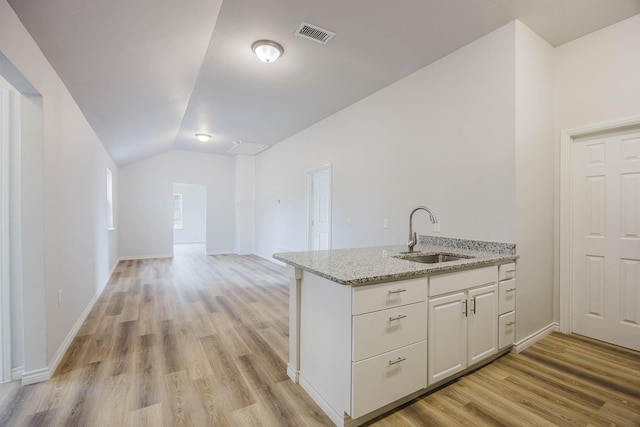 kitchen featuring visible vents, light stone countertops, lofted ceiling, white cabinets, and a sink