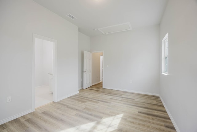 empty room with attic access, baseboards, visible vents, and light wood finished floors