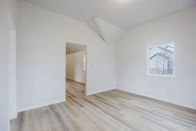 spare room with lofted ceiling, light wood-style flooring, and baseboards