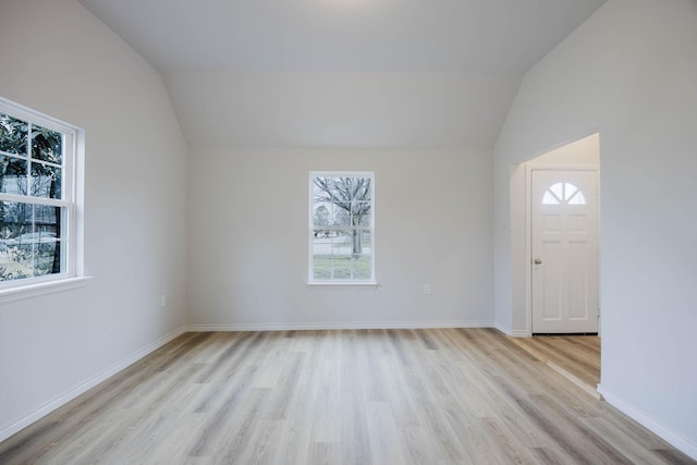 empty room featuring vaulted ceiling, light wood-style flooring, baseboards, and a wealth of natural light