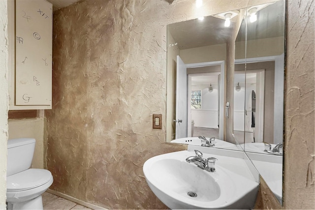 half bathroom featuring tile patterned flooring, toilet, a textured wall, and a sink