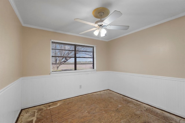 unfurnished room featuring ceiling fan, crown molding, and wainscoting