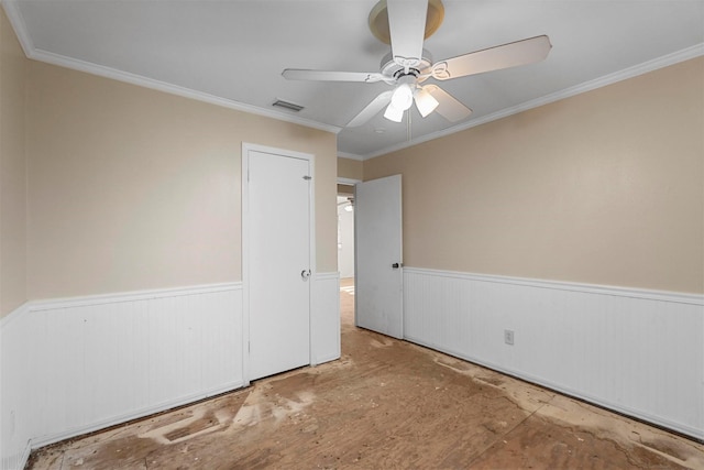 empty room with visible vents, a wainscoted wall, a ceiling fan, and crown molding