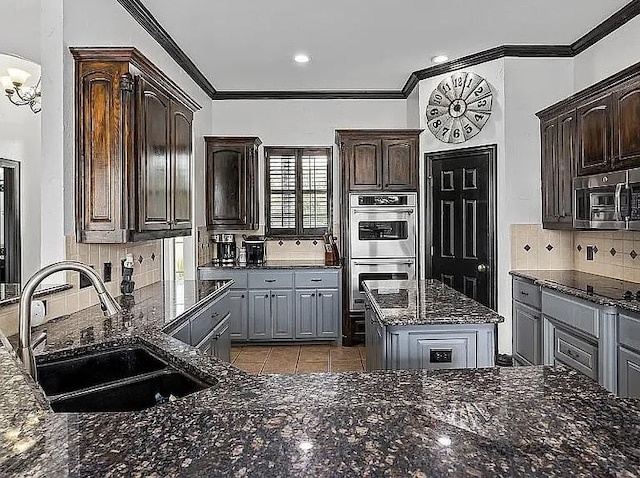 kitchen featuring dark stone countertops, ornamental molding, a sink, appliances with stainless steel finishes, and tasteful backsplash