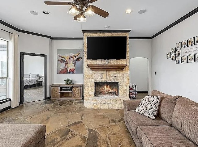 living room with crown molding, ceiling fan, a fireplace, arched walkways, and stone finish floor