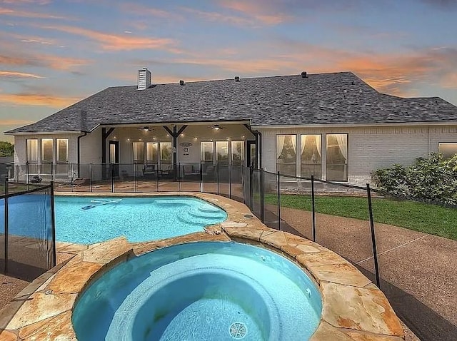 pool at dusk with a patio, fence, a ceiling fan, and a pool with connected hot tub